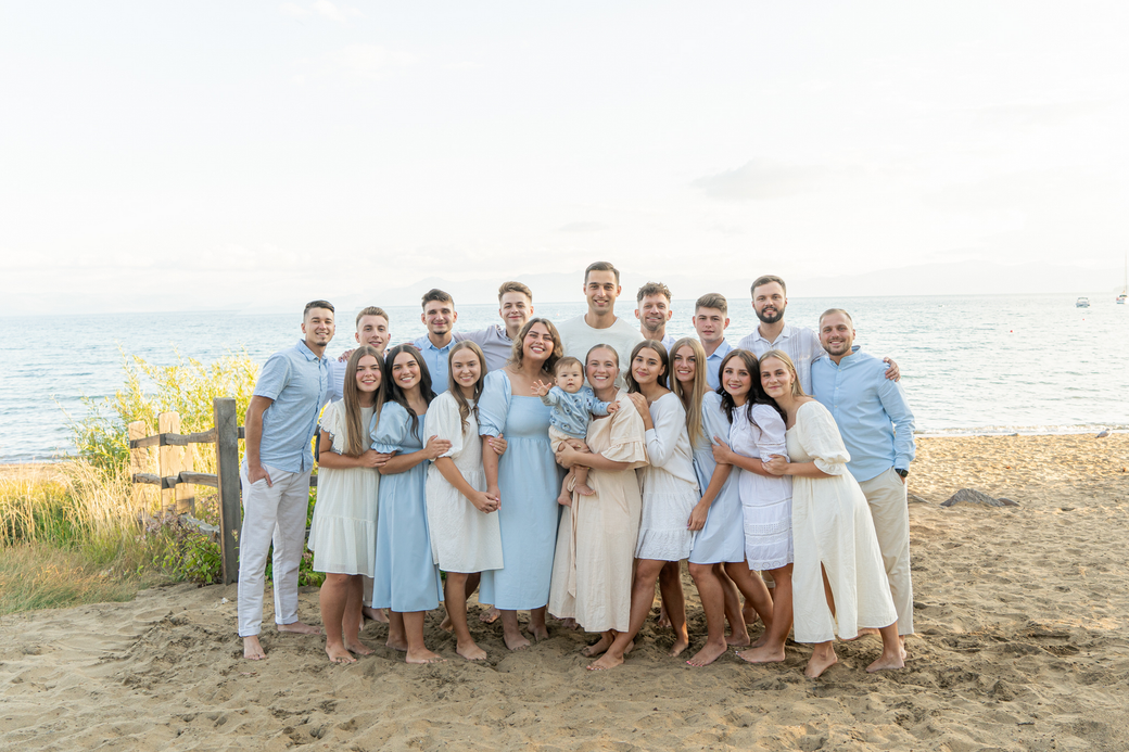A large family is posing for a picture on the beach.