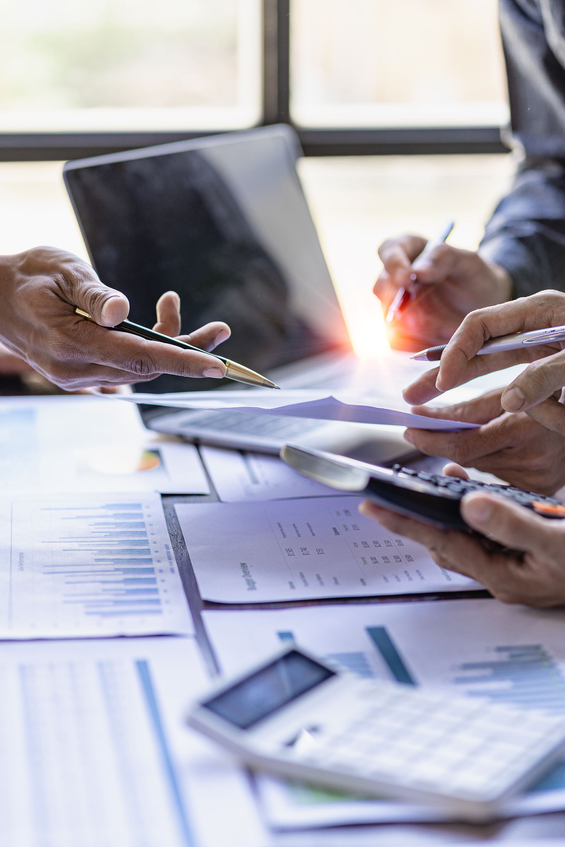 Hands reviewing financial charts and a tablet in a bright office, with calculator and pen on the desk.