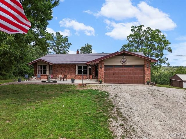 Brick ranch house with brown garage, gravel driveway, and U.S. flag in front yard