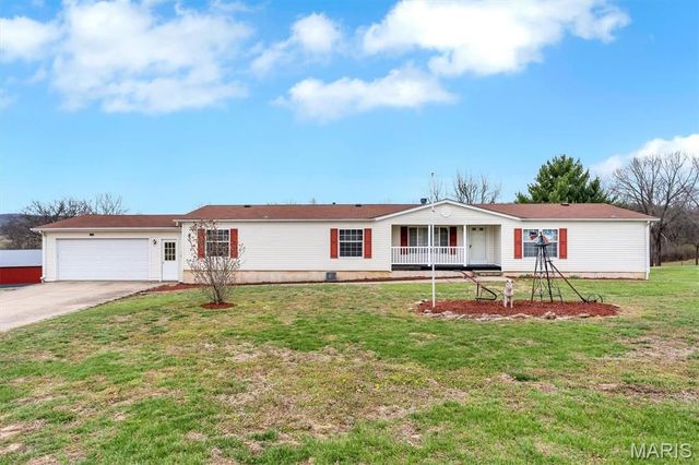 Single-story white house with red trim and a front yard under a blue sky