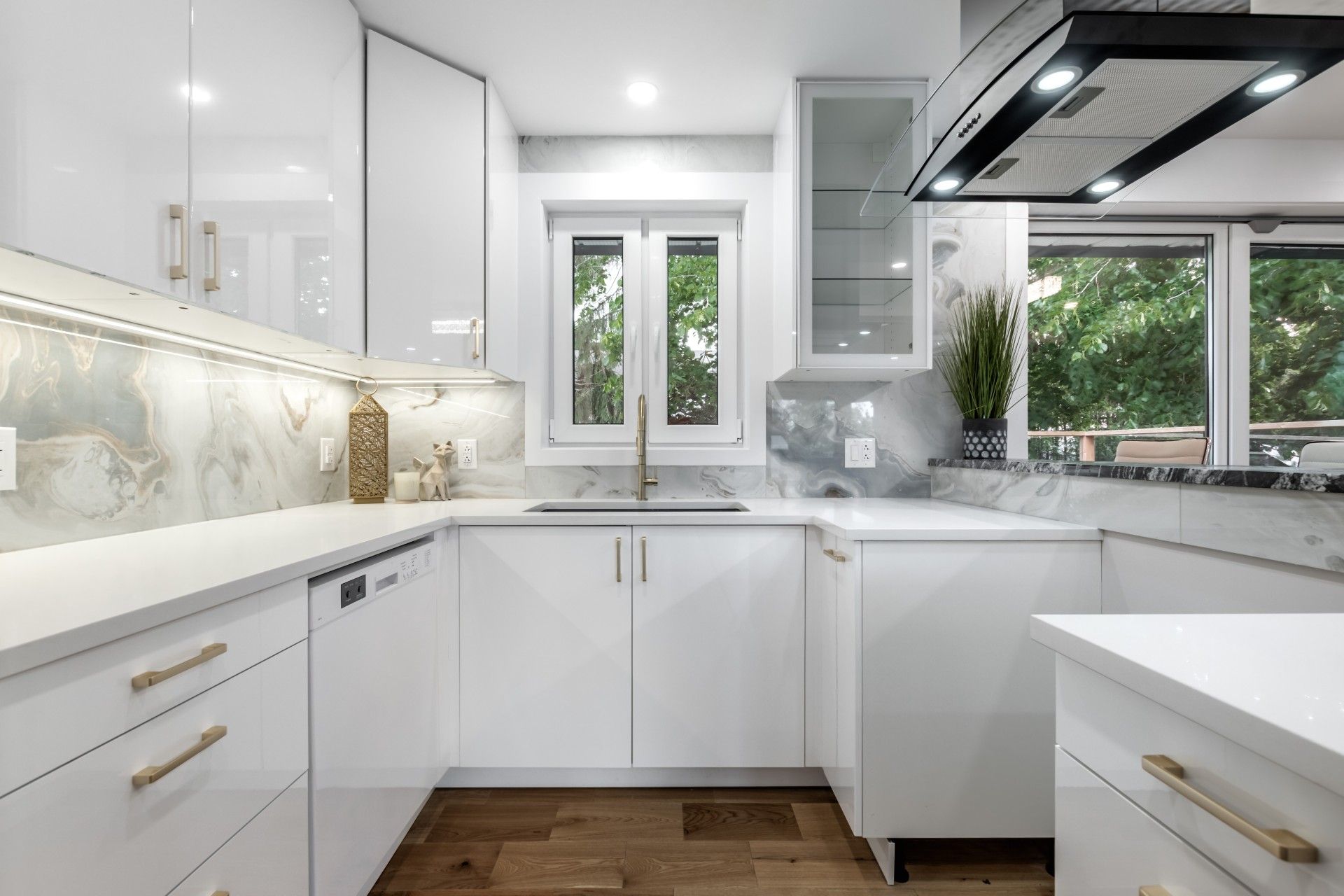 Bright modern white kitchen with marble countertops, brass accents, and a window over the sink
