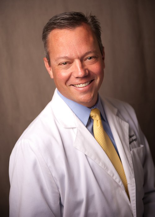 Dr. Michael Swan in lab coat leaning against a tree