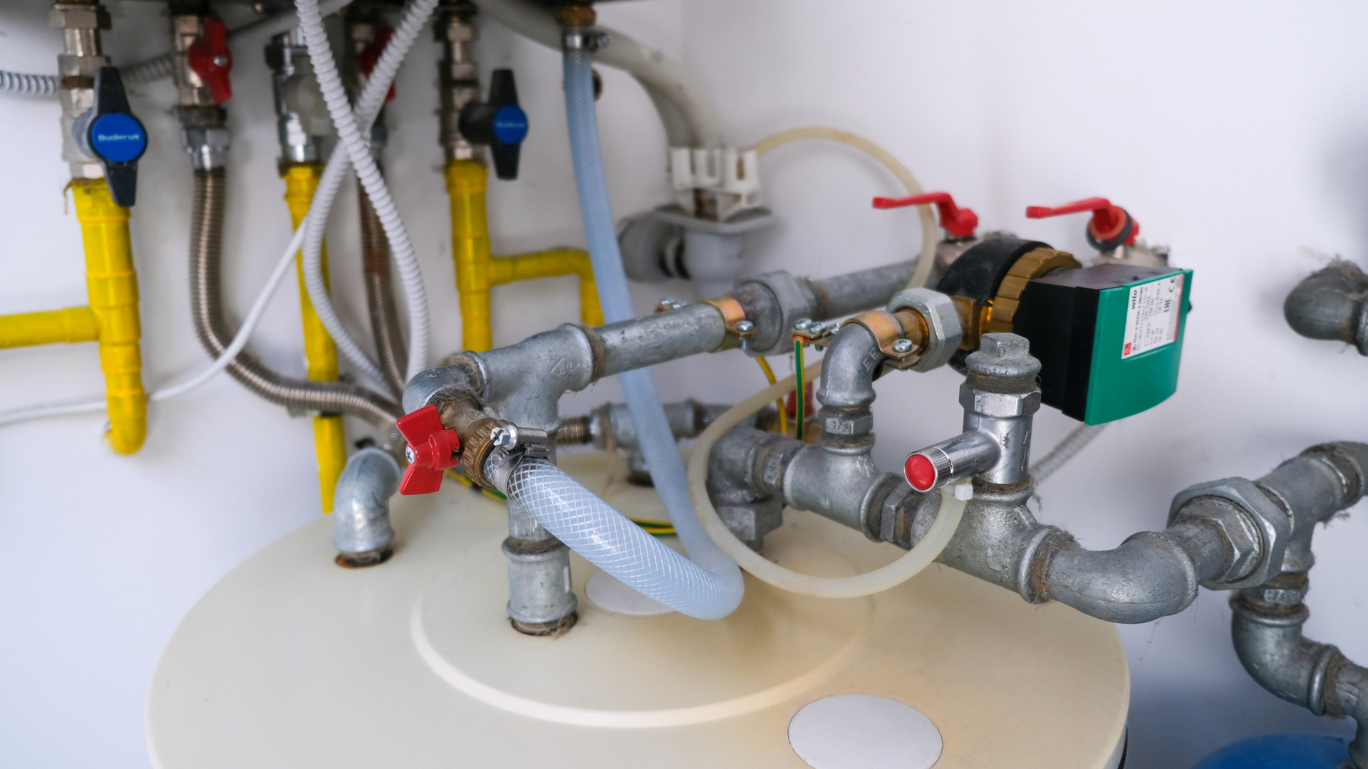 Plumbing pipes, valves, and hoses above a bathroom sink or tank in a utility installation area