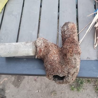 Rusty, heavily corroded metal pipe fitting on a gray wooden deck.