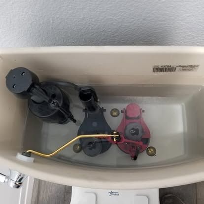 Open toilet tank with black and pink flush valves and a gold water supply tube inside