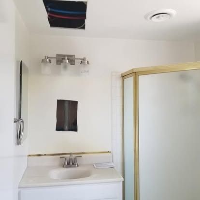 Small white bathroom with sink, mirror, light fixture, and gold-framed shower enclosure.