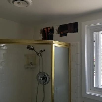 Small bathroom shower with gold trim, frosted glass door, white tile, and a window on the right.