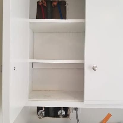Open white cabinet with shelves; pipes and valves visible at the bottom.