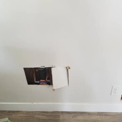 Cutout in a white wall near the baseboard with an open panel, exposing wiring and a blue box.