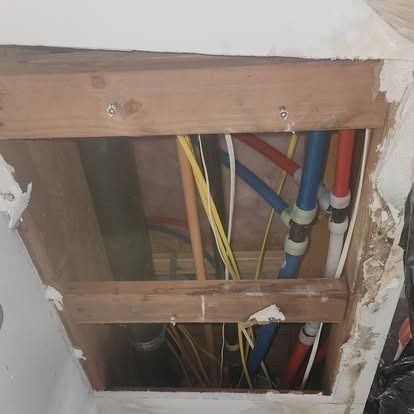 Open wall cavity with exposed colored plumbing and electrical pipes between wooden studs