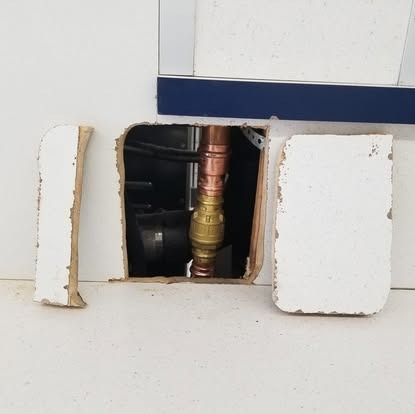 Open wall with exposed copper pipe and brass valve behind removed white panels