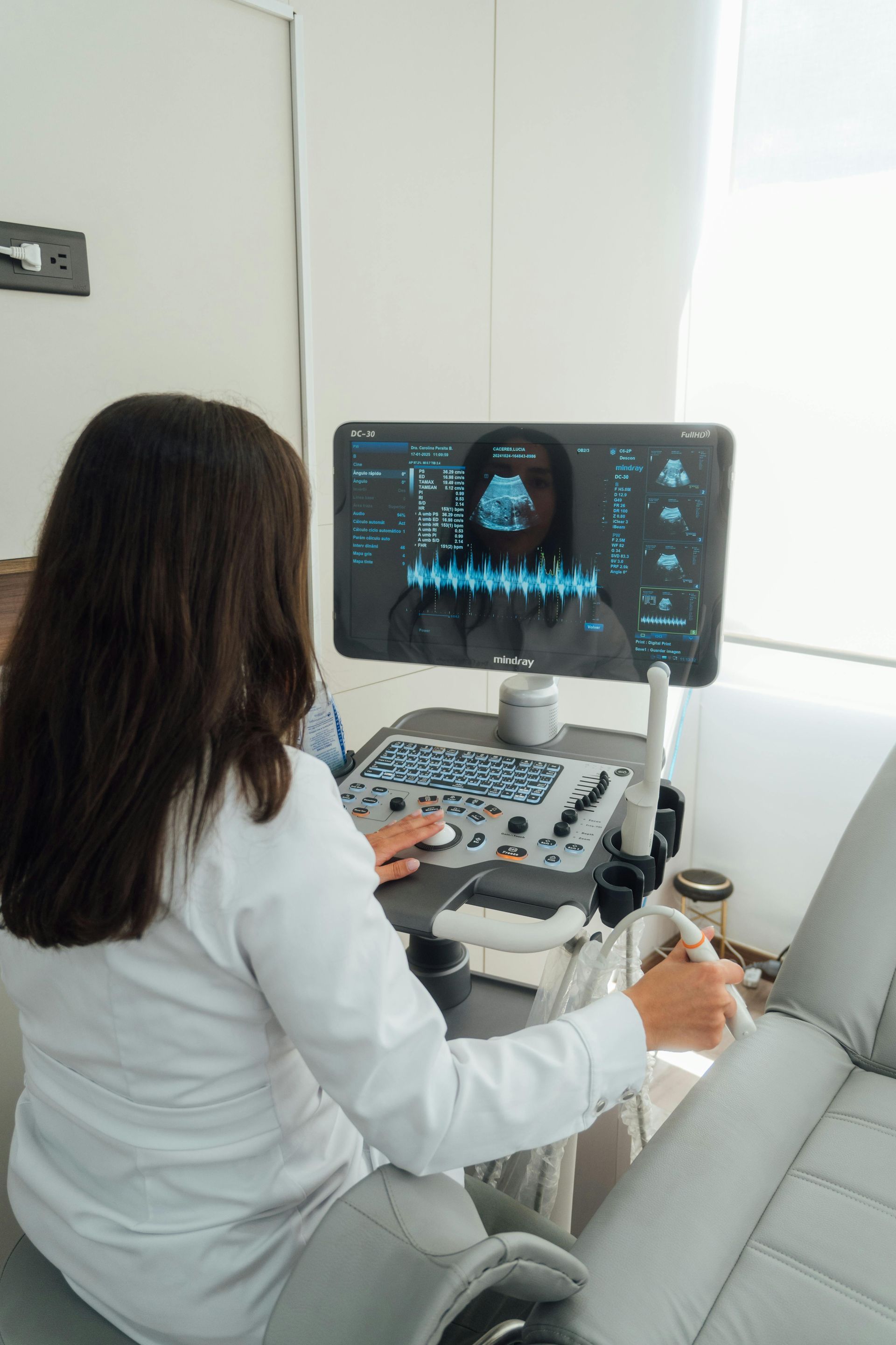 Technician using an ultrasound machine in a clinical room, viewing a patient scan on the monitor.