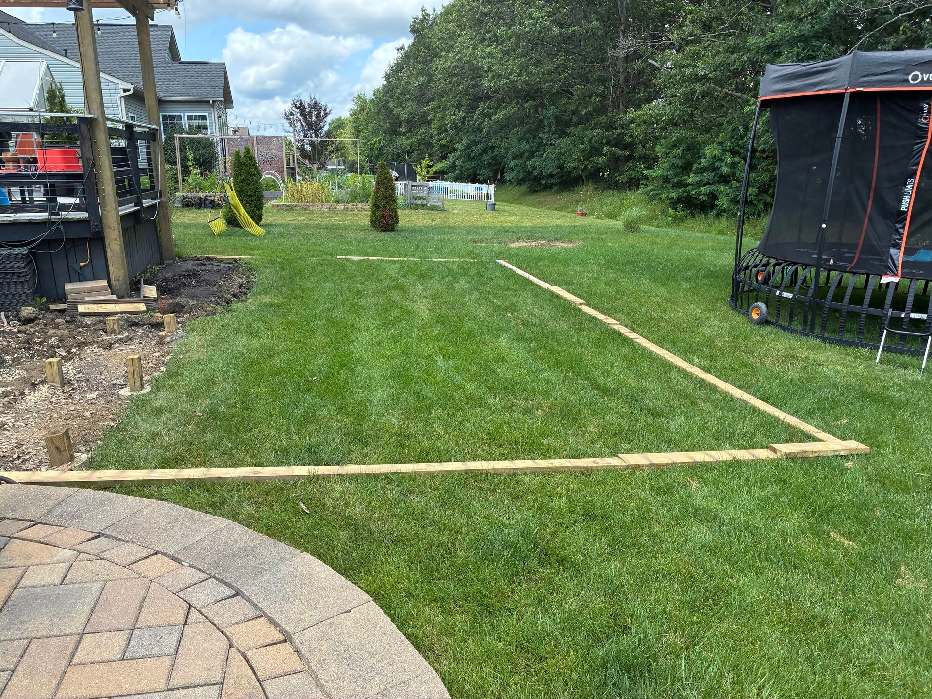 Wooden frame on grass, outlining a rectangular area in a backyard, near a deck and tent.
