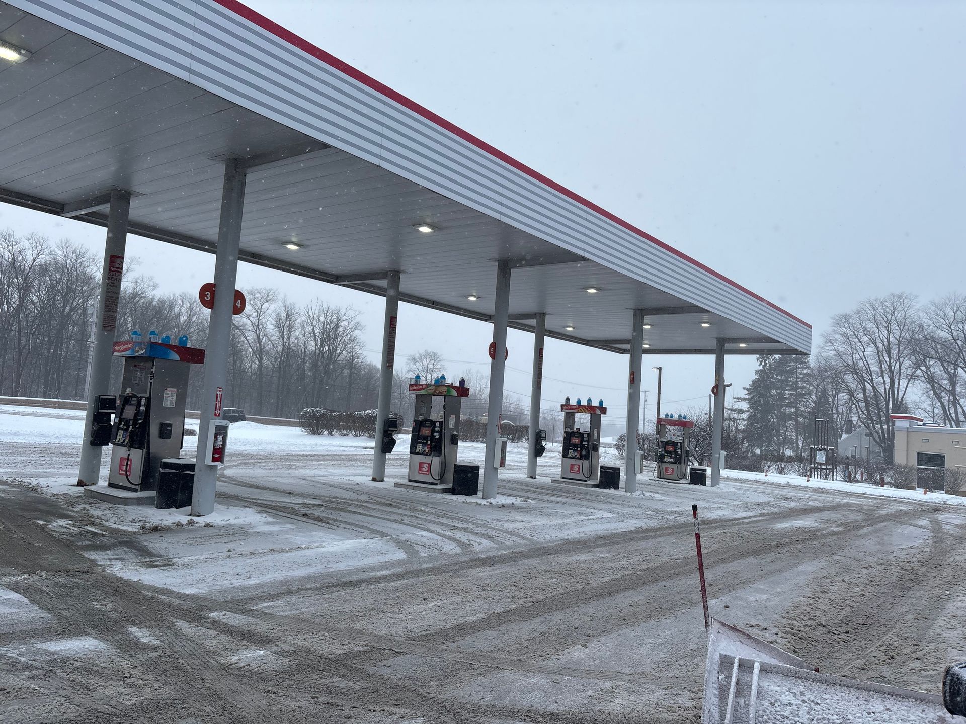 Gas station canopy and pumps covered in snow. Gray overcast sky.