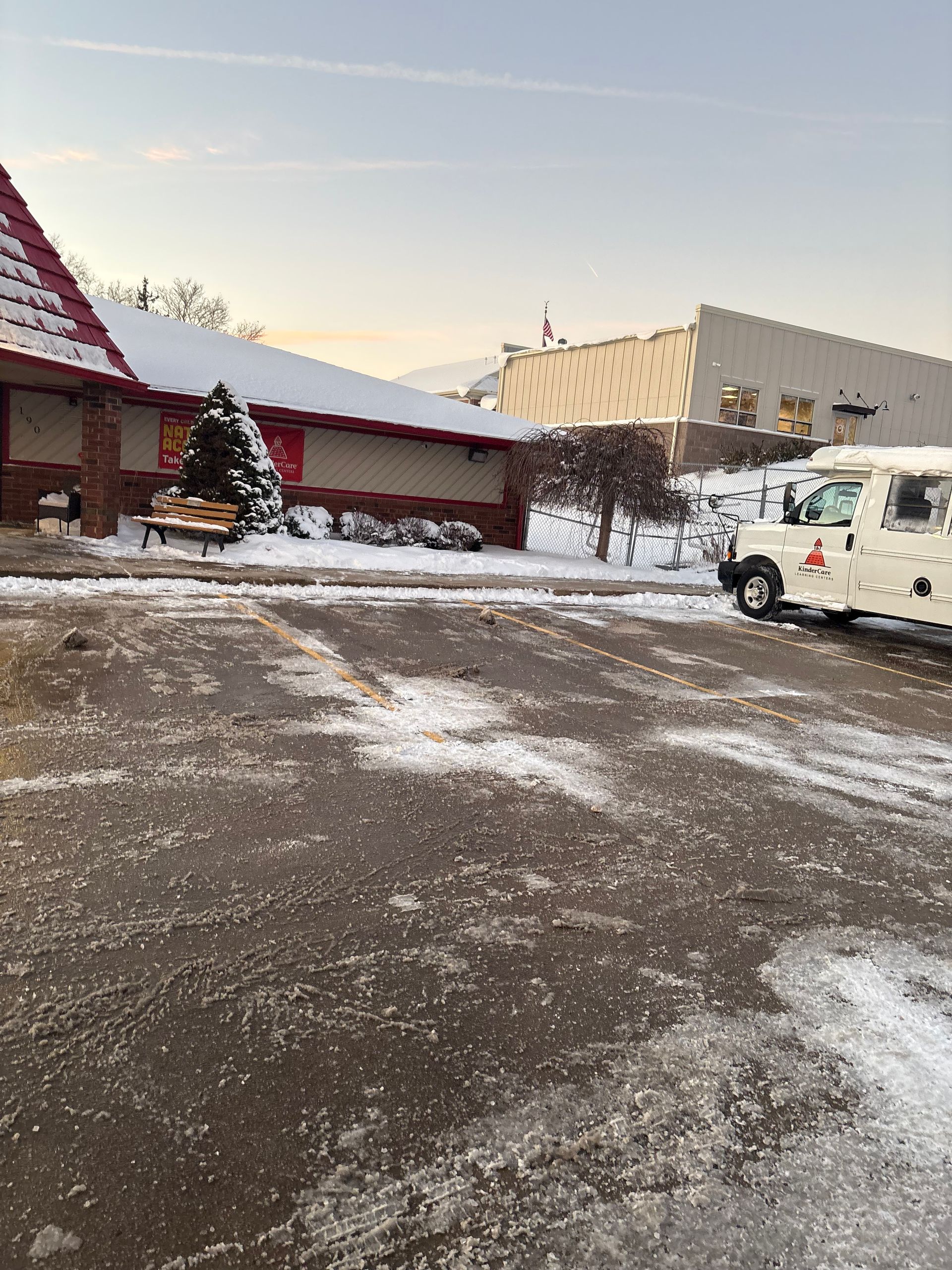 Snowy parking lot with a building, decorated with a small Christmas tree, and a white utility truck.