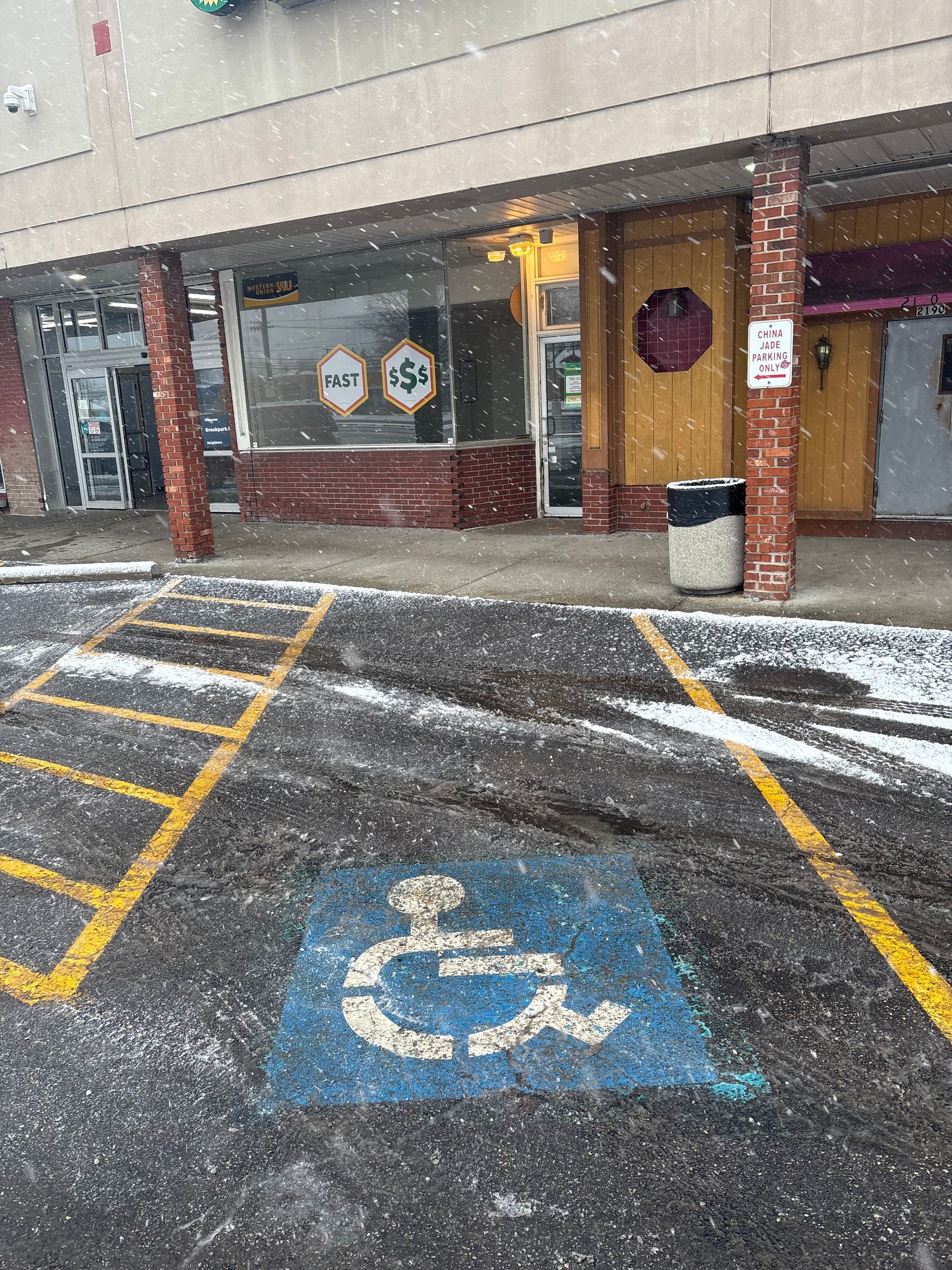 Blue handicap parking symbol in a snow-covered parking lot in front of storefronts.