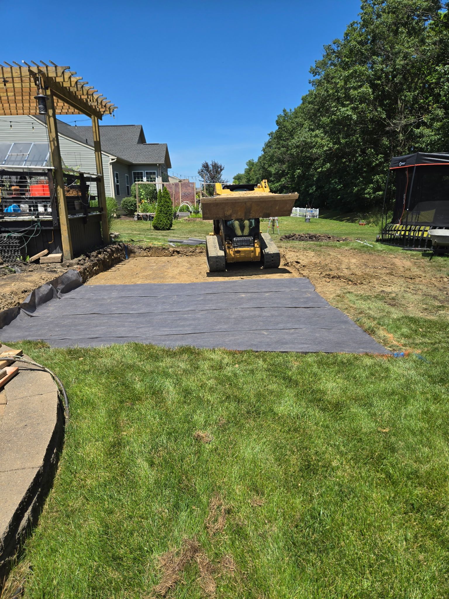A skid steer loader is working on a construction site with a new patio area, with a layer of landscaping fabric.