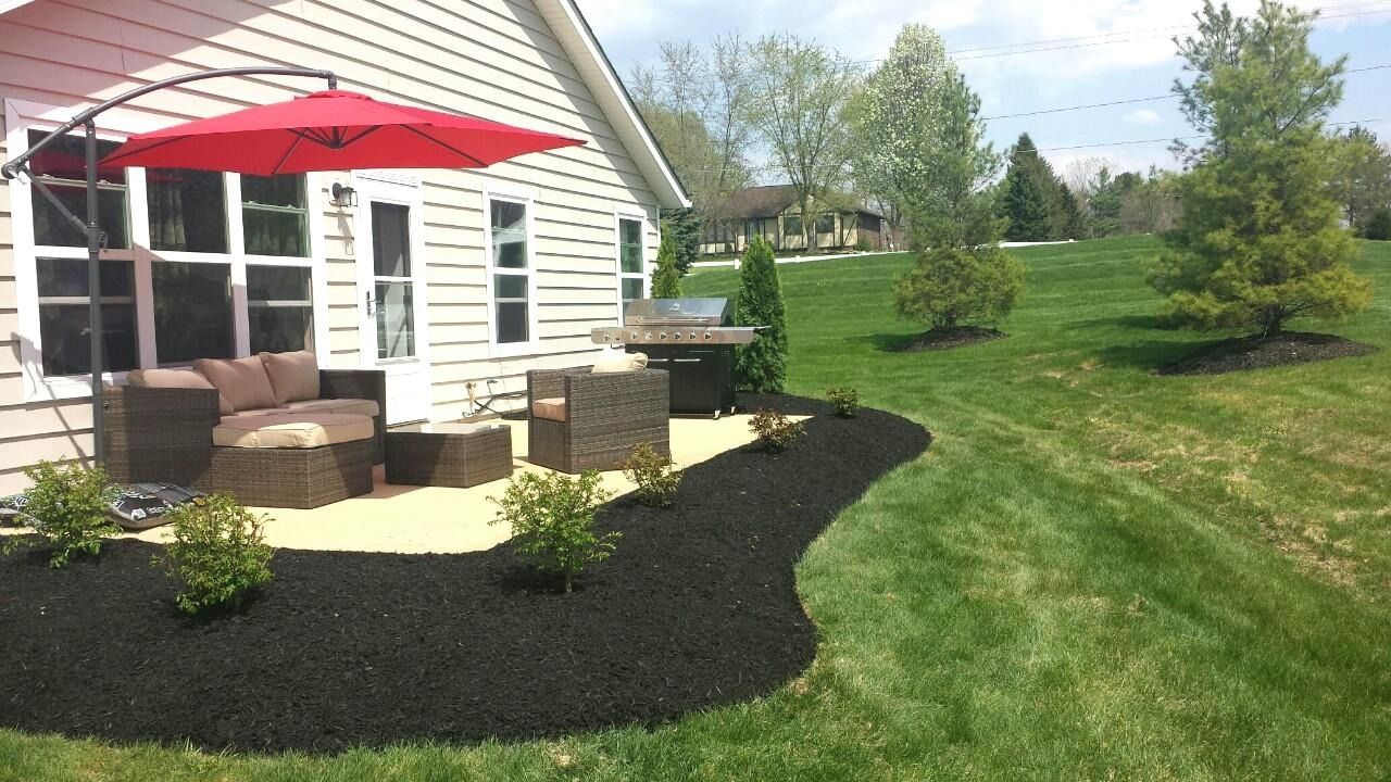 Outdoor patio with wicker furniture, red umbrella, and black mulch border.