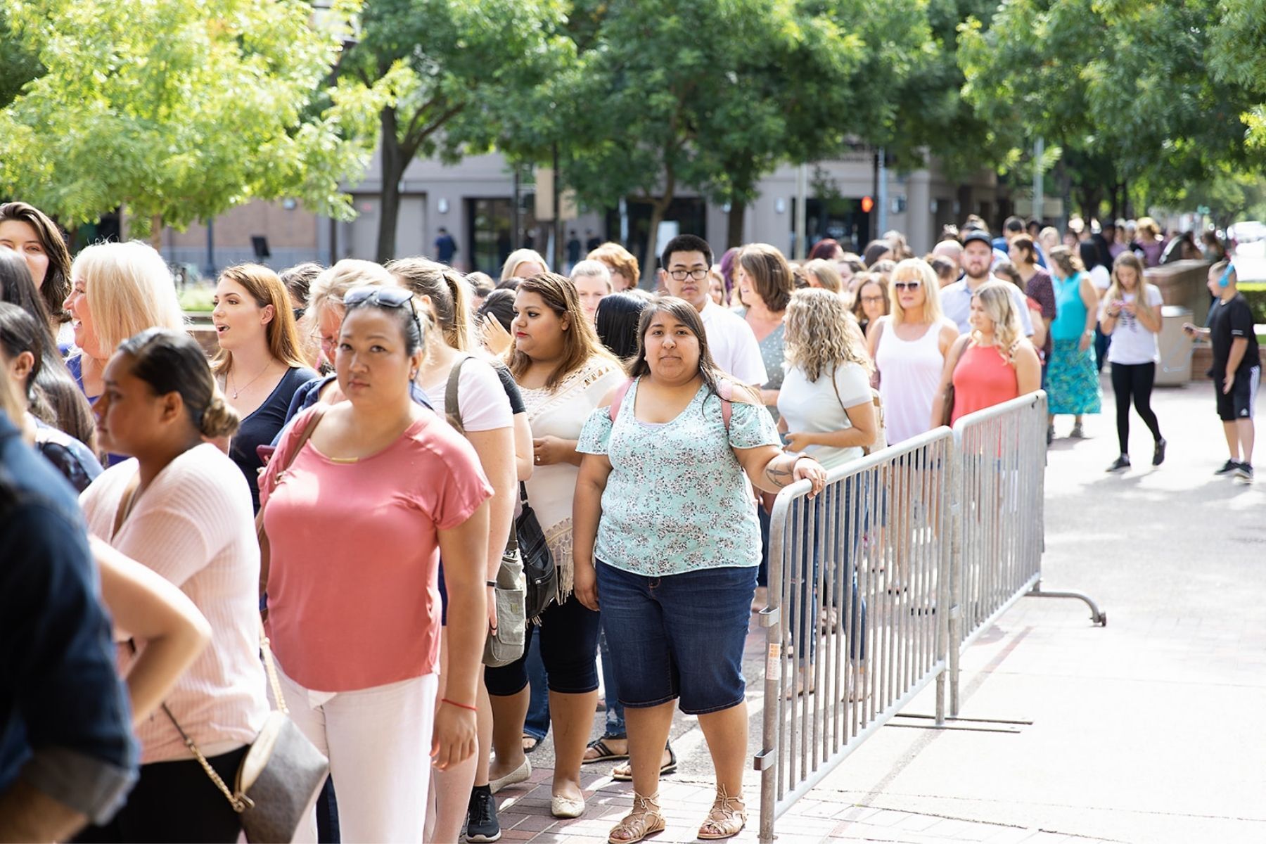A large group of people are standing in a line behind a fence.