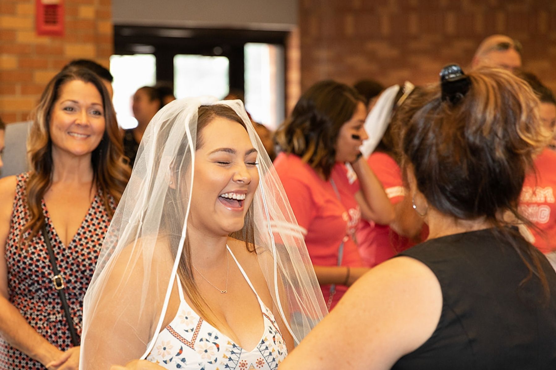 A woman in a wedding dress and veil is laughing with another woman.