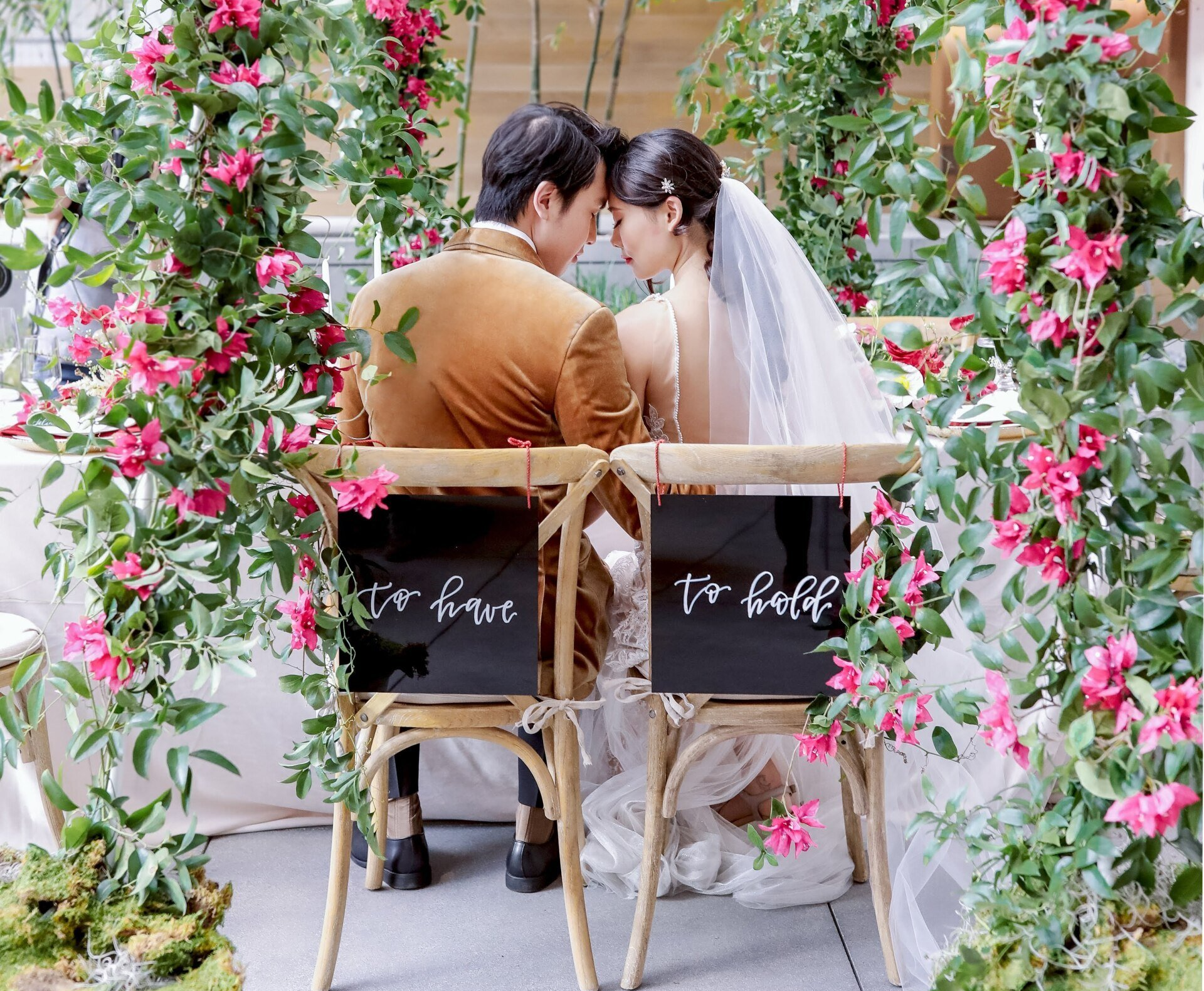 A bride and groom are sitting in chairs with a sign that says `` to have ''.