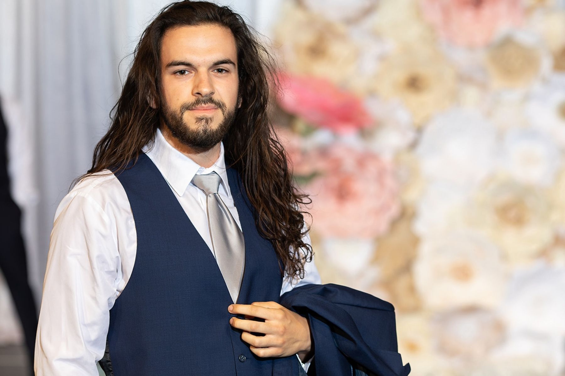 A man with long hair and a beard is wearing a suit and tie.