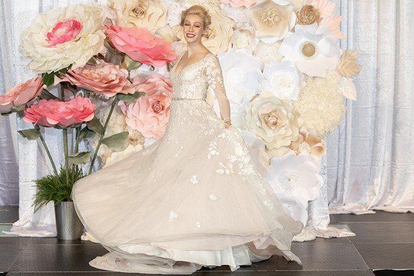 A woman in a wedding dress is standing in front of a wall of paper flowers.