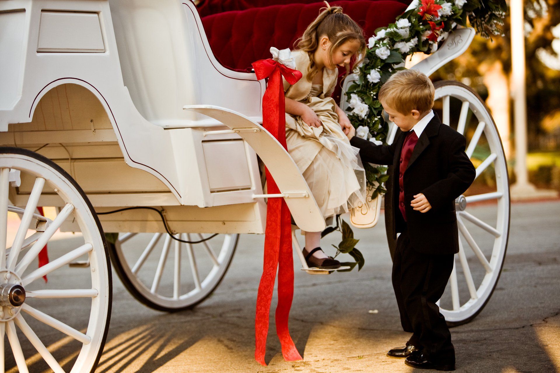 A boy and a girl are standing next to a white horse drawn carriage