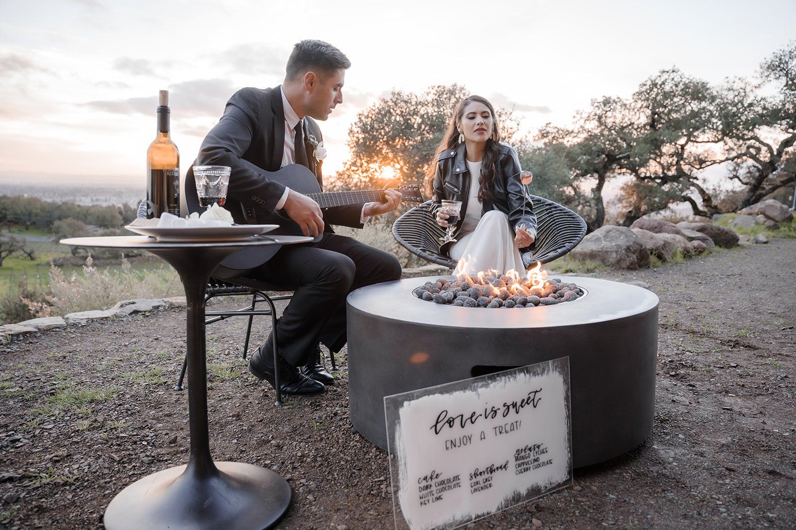A man and a woman are sitting at a table next to a fire pit.