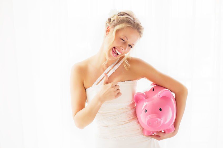 A woman in a wedding dress is holding a pink piggy bank and a toothbrush.
