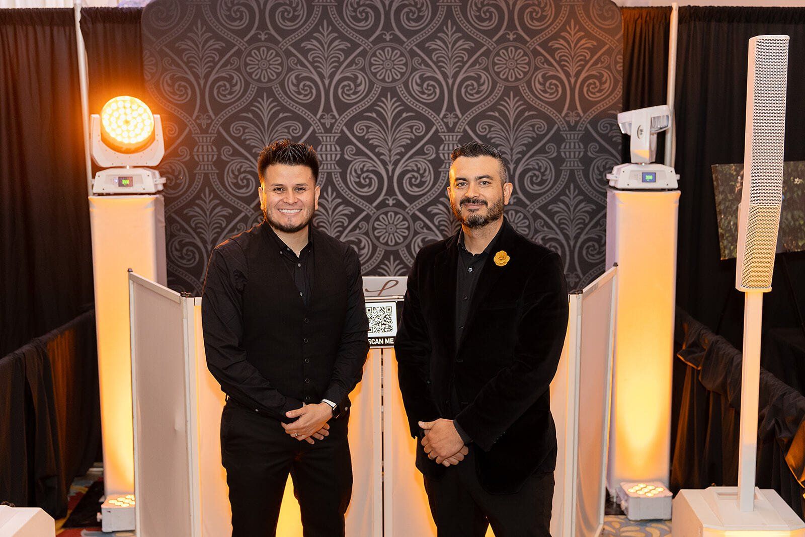 Two men are standing next to each other in front of a dj booth.