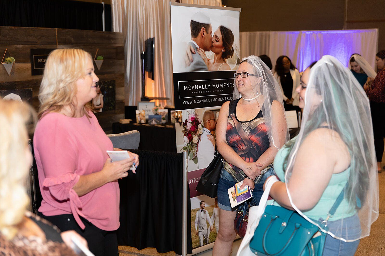 A group of women are standing in a room talking to each other . one of the women is wearing a veil.