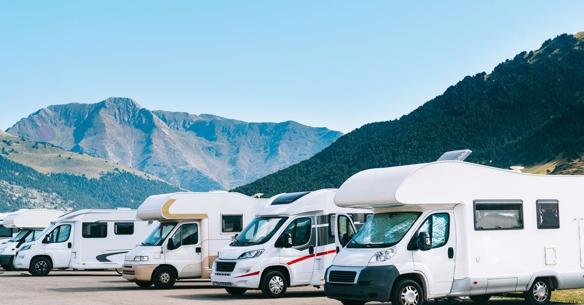 Several white RVs of various sizes parked in a long row. There are mountains in the background.