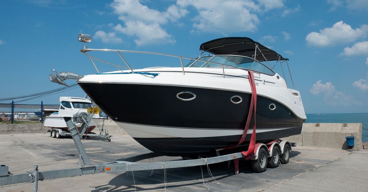 A large black and white boat sitting on a metal trailer with wheels in front of a body of water on a