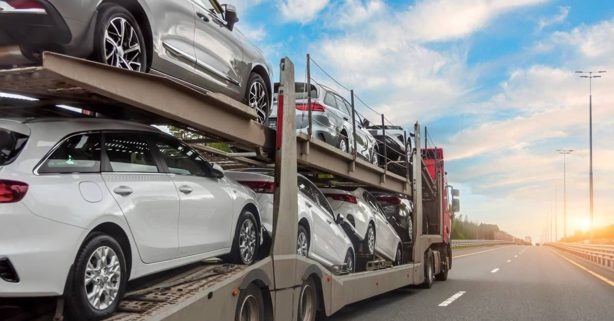 A truck with a red cab hauling cars on a two-story trailer while driving down the highway on a sunny day.