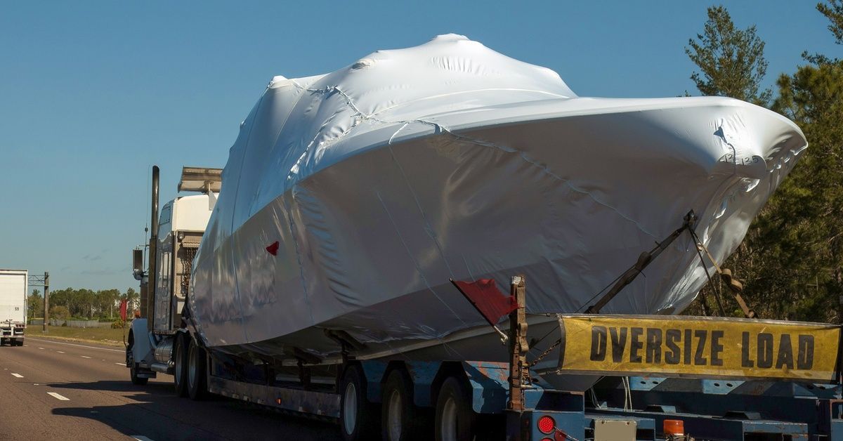 A semi-truck transporting a covered boat with an 'oversize load' sign on the back of the trailer.