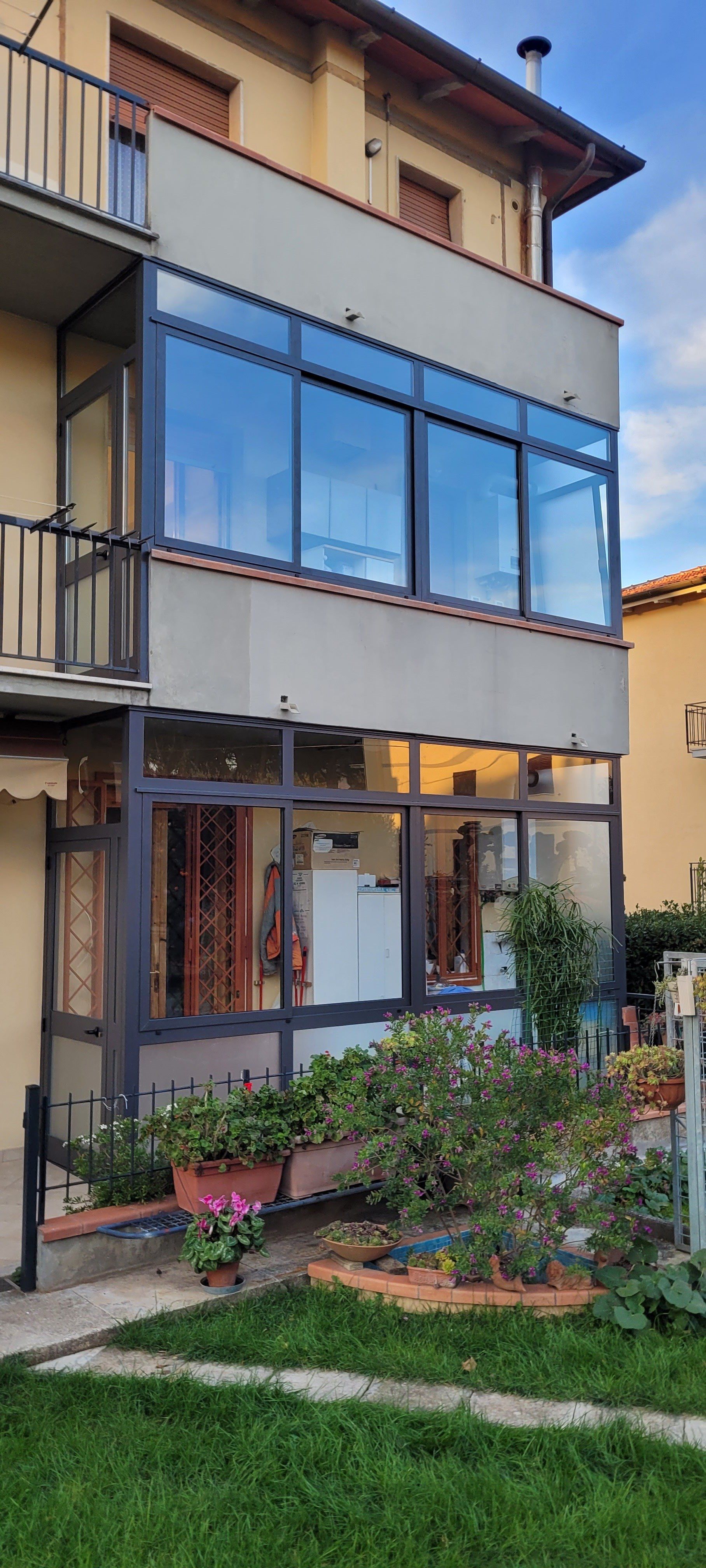 Casa residenziale con un ampio balcone vetrato e un piccolo giardino antistante.