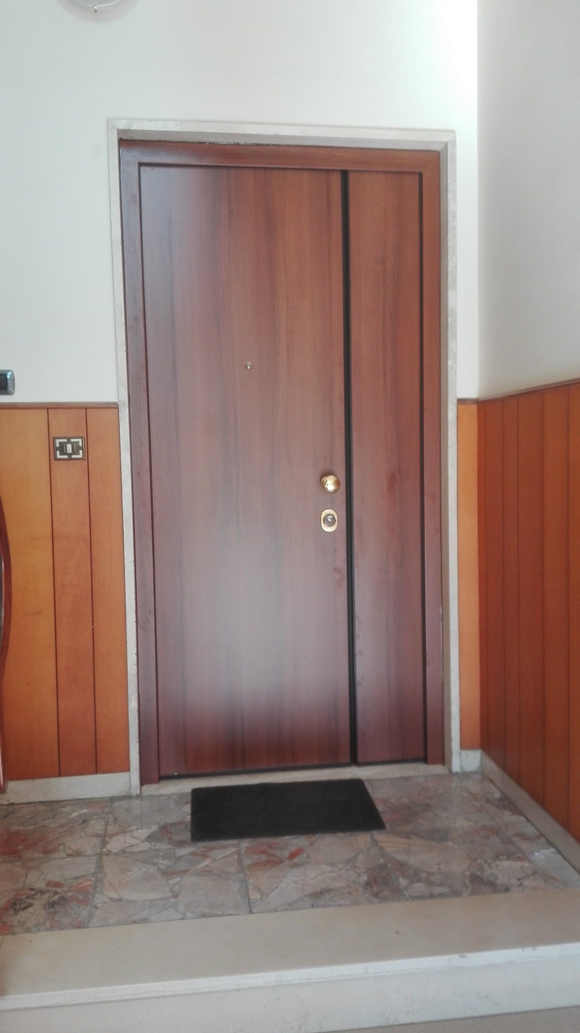 Porta d'ingresso in legno con zerbino nero in un ingresso piastrellato