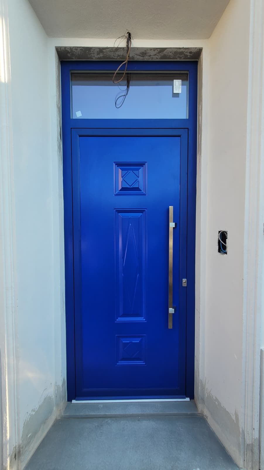 Porta d'ingresso di un blu brillante in uno stretto corridoio bianco con una piccola finestra a lunetta sopra.