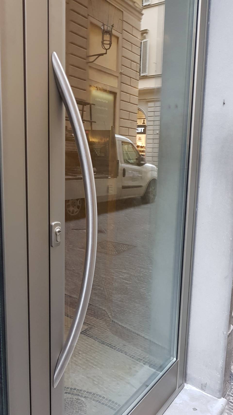 Porta del negozio in vetro con maniglia in metallo curva che riflette la strada e un'auto parcheggiata
