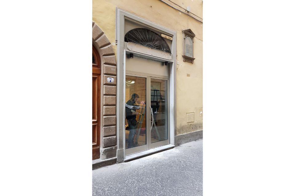 Vetrina con porta e finestra in vetro su una strada stretta, facciata beige e arco a strisce sopra l'ingresso.