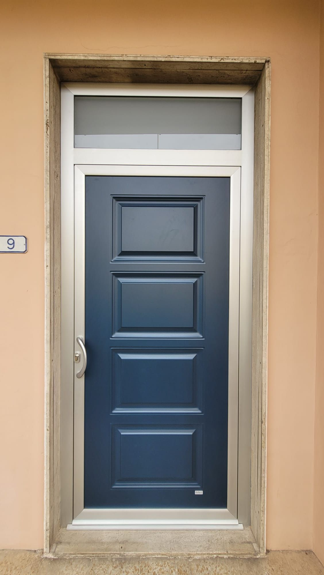 Porta d'ingresso blu con sopraluce satinato incastonata in una parete beige