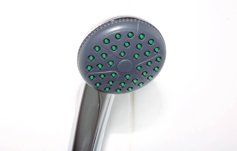 Gray and chrome showerhead with green nozzles against a white wall.