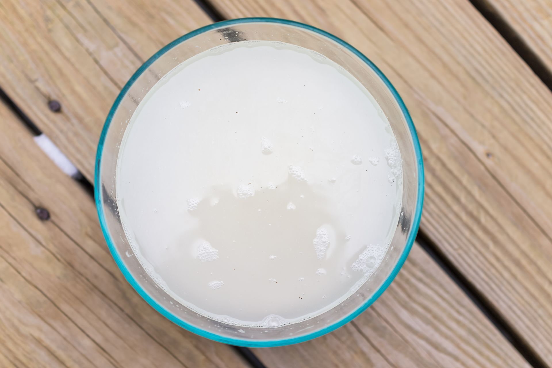 Clear liquid drink in a teal-rimmed glass on a wooden surface, likely a margarita.