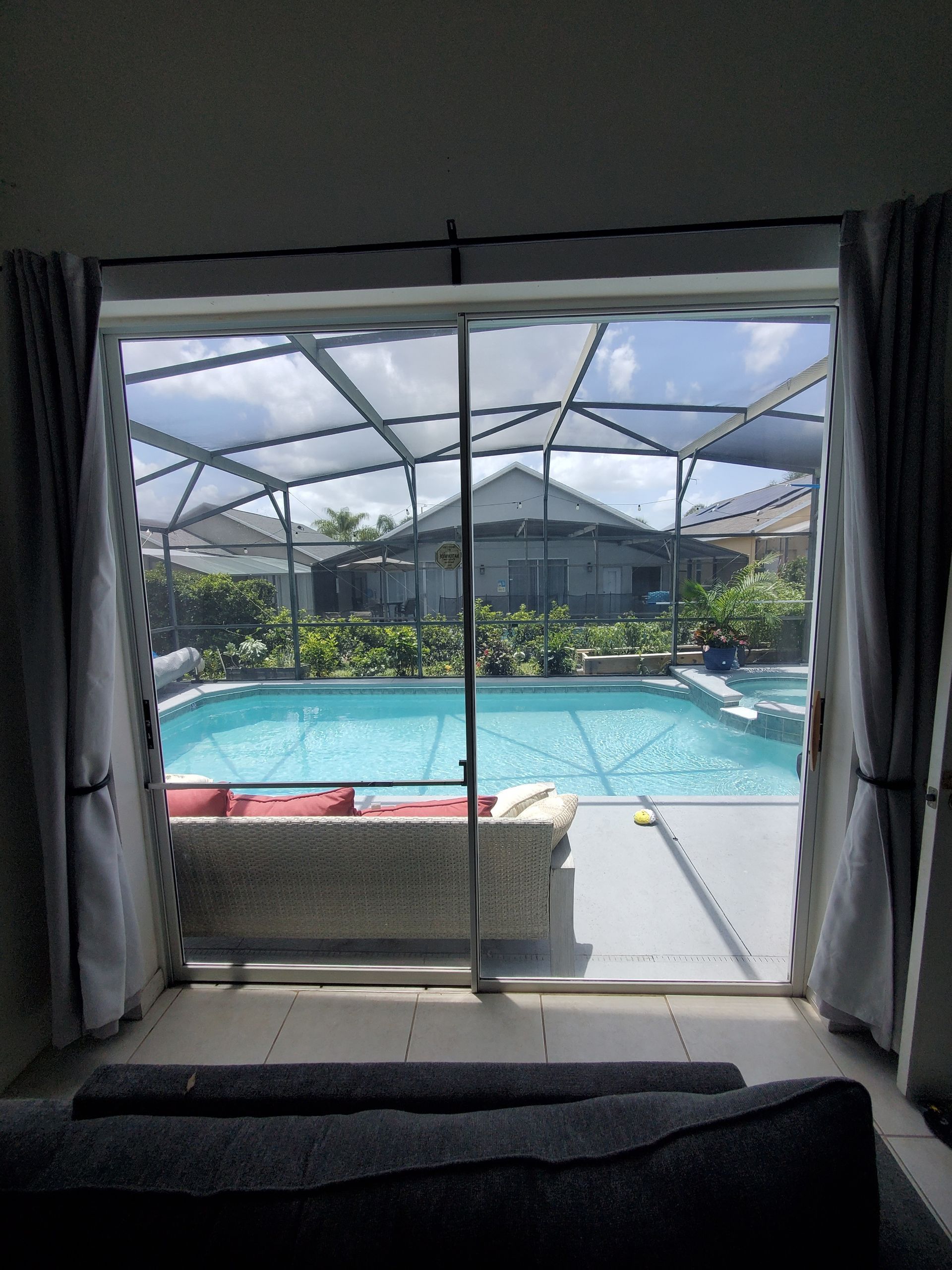 View from indoors looking out a sliding glass door at a screened-in pool patio and a backyard with green landscaping.