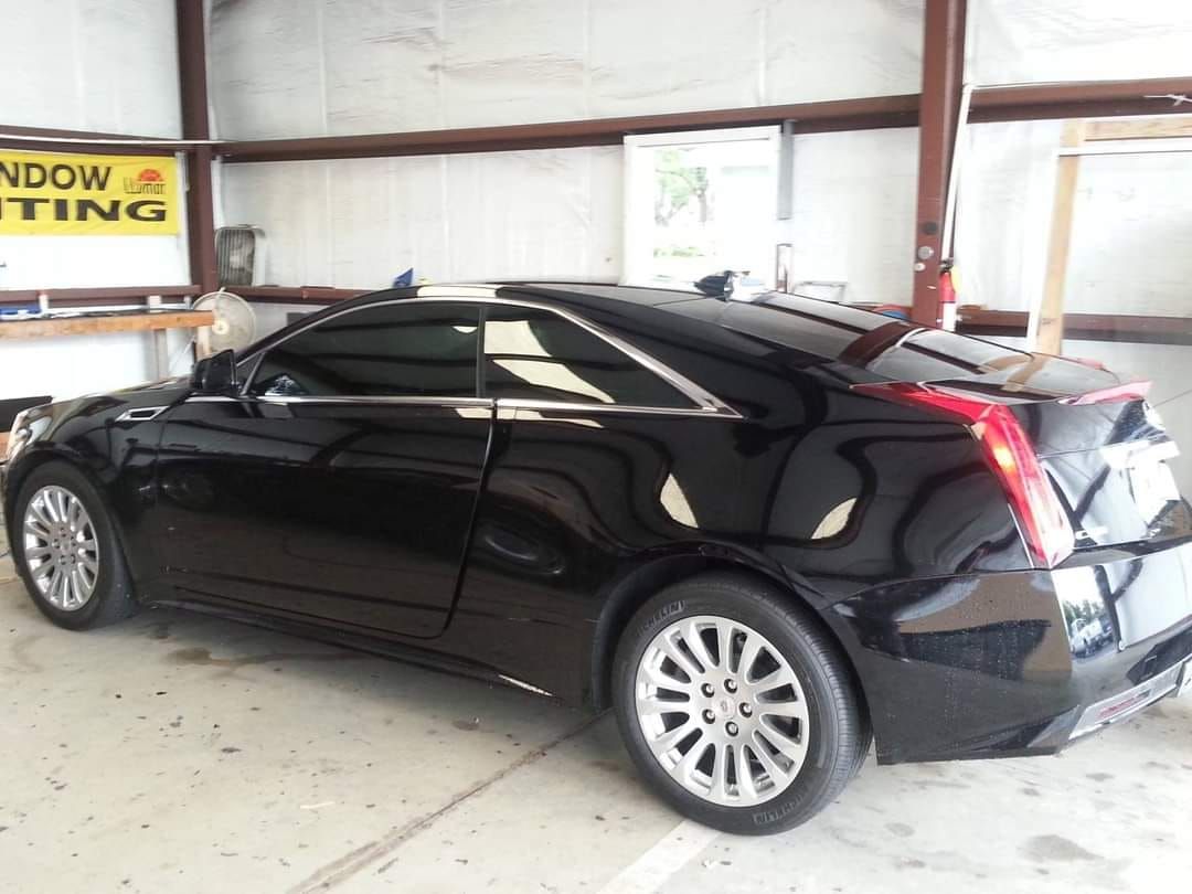 A black car is parked in front of a sign that says window tinting