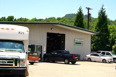 Bus, pickup truck, and cars outside a metal garage on a sunny day