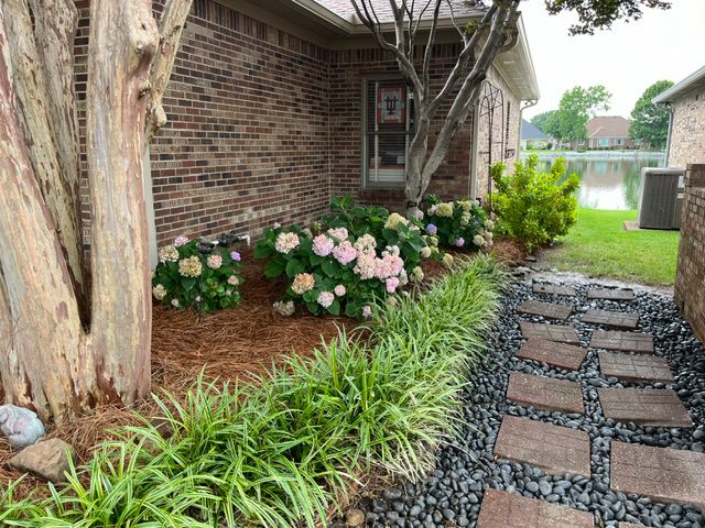 A brick house with a walkway leading to it and flowers in front of it.