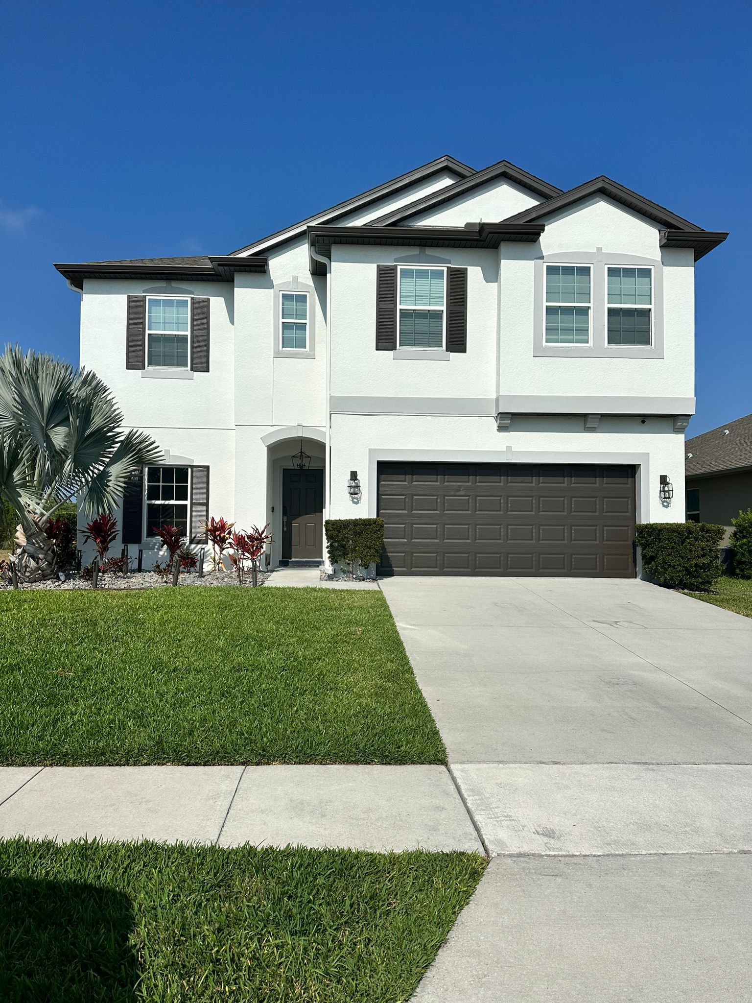 Two-story white house with a black garage door, driveway, and green lawn under a clear sky