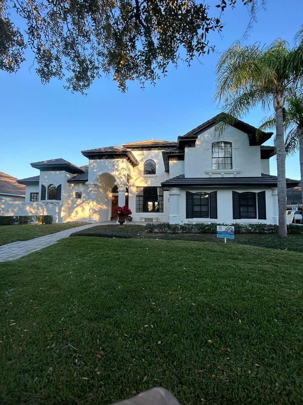 Large white house with stone accents and a red car parked in the driveway at dusk.